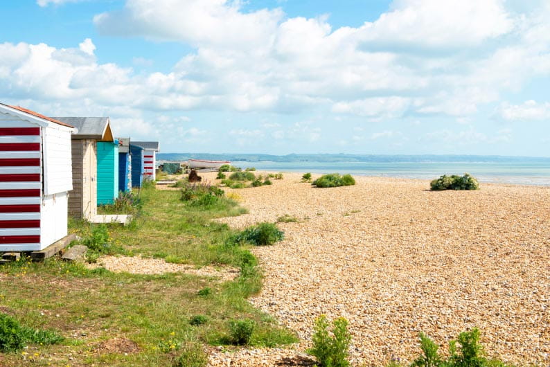 Colourful beach huts looking out over a shingle beach near Romney in Kent