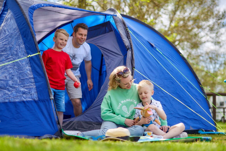 Family sat on the grass outside their tent