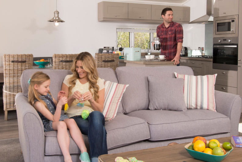 Mum and daughter sat on sofa with dad in the kitchen