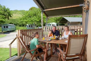 A family sitting out on the veranda of their glamping tent at Nodes Point Holiday Park