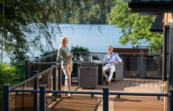 A couple relaxing on the veranda of their luxury lodge in the Lake District