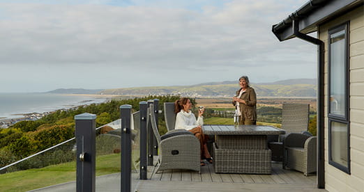 A family enjoying drinks on the veranda of their lodge at Brynowen Holiday Park in Wales
