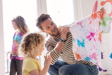 father holding up a tie dyed tshirt to his toddler
