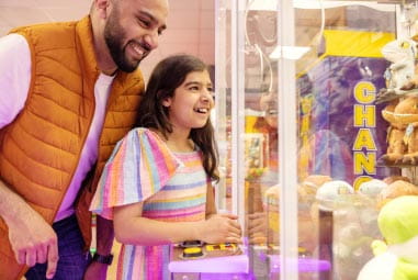 a child playing on an amusement arcade with her father
