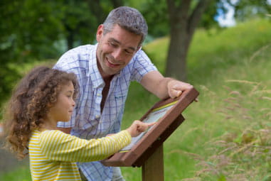 father looking at a wildlife notice board with his daughter