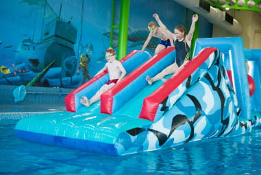 children going down an inflatable slide in an indoor pool