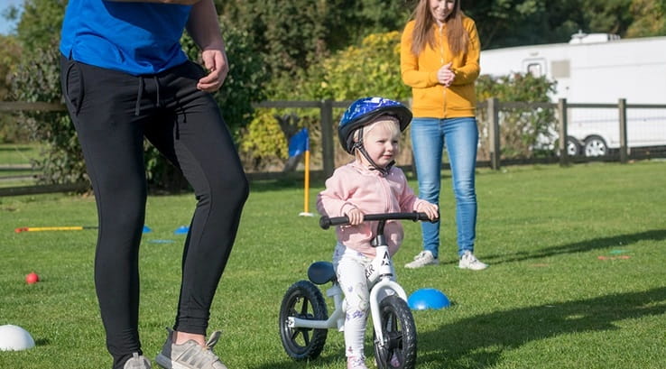 A little girl riding a bike whilst being supervised