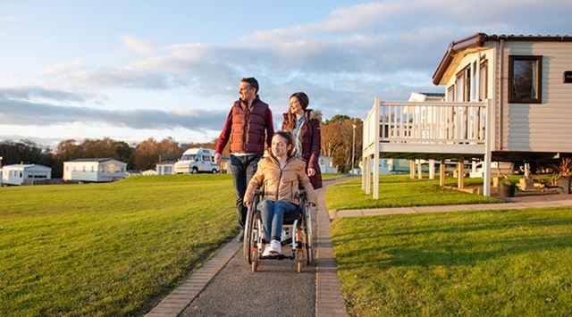 Parents pushing their teenage daughter in a wheelchair around a holiday park