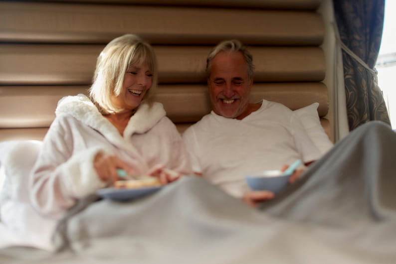 Couple sat in bed smiling in dressing gowns