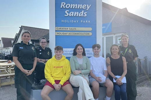 Group of people sat underneath Romney Sands entrance sign