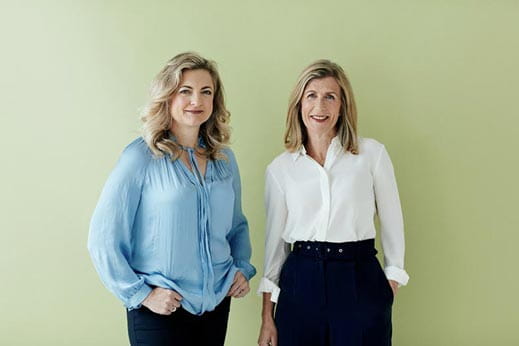 Two ladies smiling with hands in trouser pockets