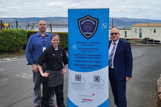 Three members of staff stood next to a pull up banner