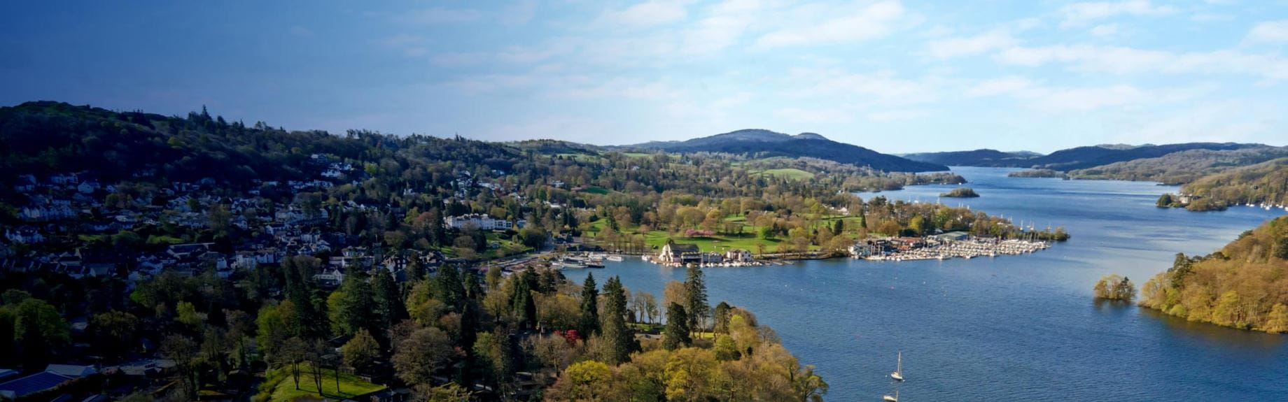 A scenic aerial view of a lake surrounded by greenery, trees, and hills