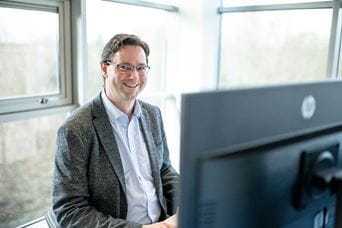 Man sat behind computer screen smiling for the camera