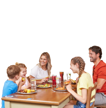 Family of five sat around a wooden table eating, drinking and smiling