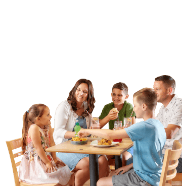 Family of five sat around a wooden table eating, drinking and smiling