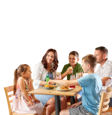 Family of five sat around a wooden table eating, drinking and smiling