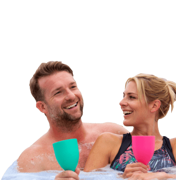 Man and woman sat smiling in a hot tub holding green and pink plastic wine glasses