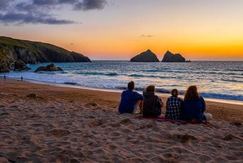 People sat on Holywell Bay Beach watching the sunset