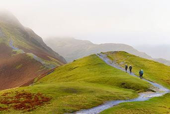 Hikers heading up the path along Cats Bells in the Lake District on a misty autumn day