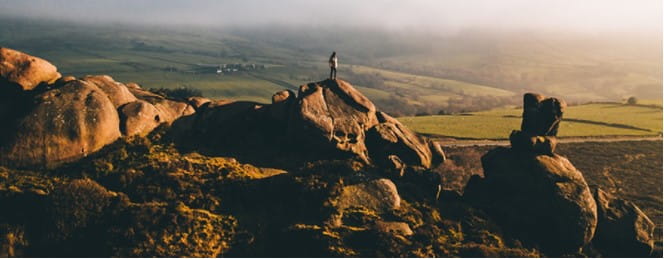 A man standing on rocks in the countryside at sunrise