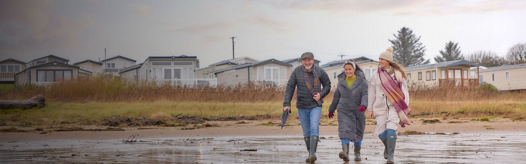 A family walking along the beach with a Parkdean holiday park visibile in the background