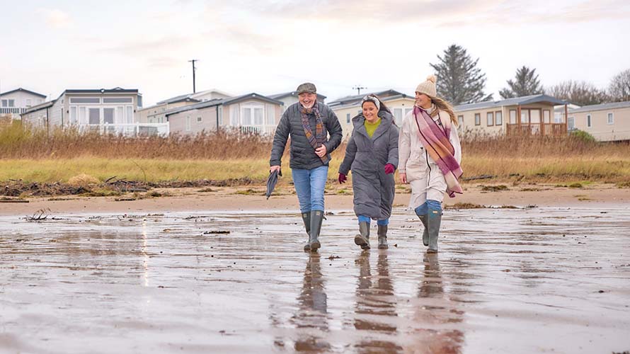 A family walking along the beach with a Parkdean holiday park visibile in the background