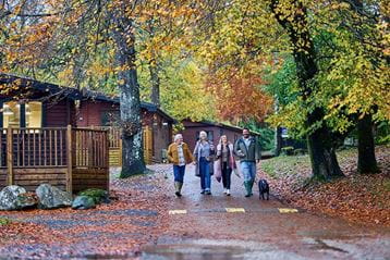 A family walking their dog through White Cross Bay Holiday Park on an autumn day