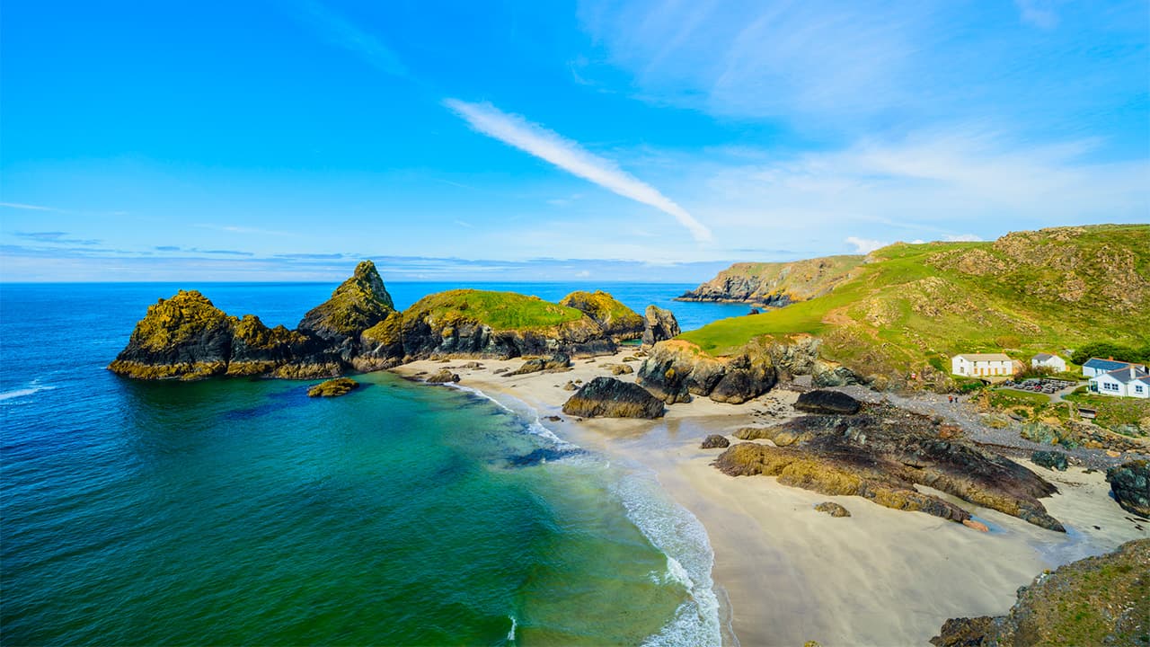 A view over the blue waters and white sand of Kynance Cove in Cornwall on a summers day