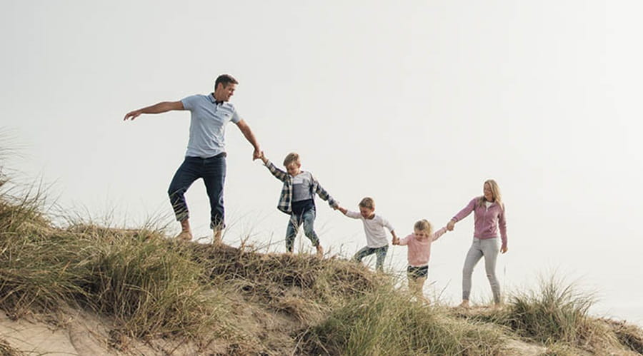 A family walking along grassy sand dunes holding hands