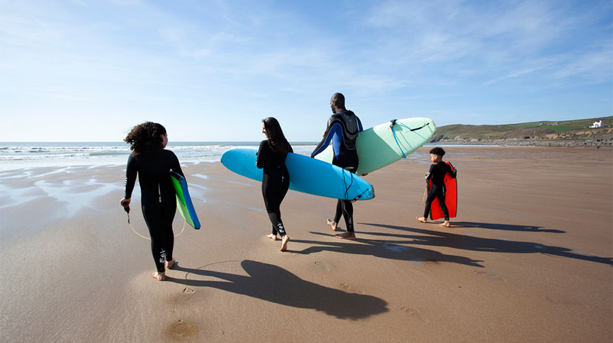 A family carrying surfboards on Croyde Bay Beach in Devon