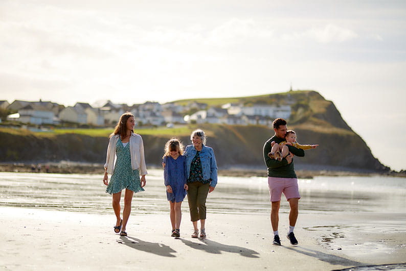 A family enjoying a summer stroll along a beach in Wales