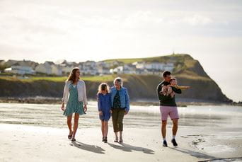 A family enjoying a summer stroll along a beach in Wales