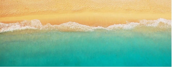 An aerial view of bright blue waves crashing onto golden sand
