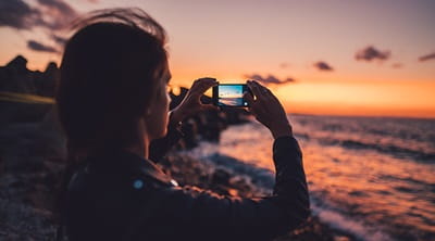 Woman taking a photo of a sunset on her phone