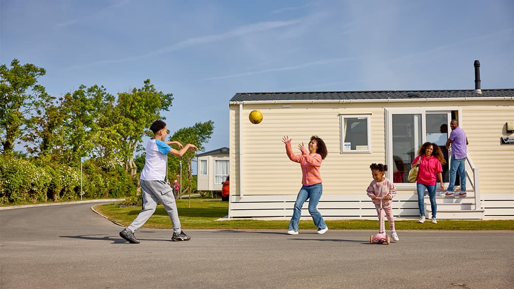 A family playing with a ball outside of their caravan holiday accommodation