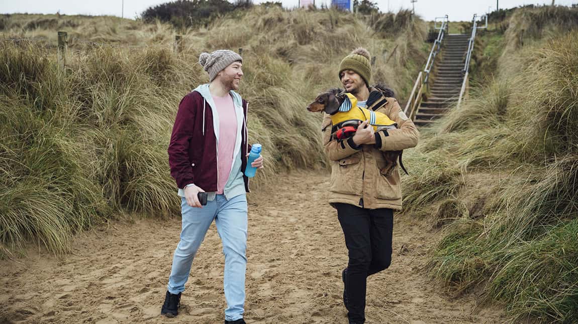 A couple carrying their dog down to the beach for a winter walk
