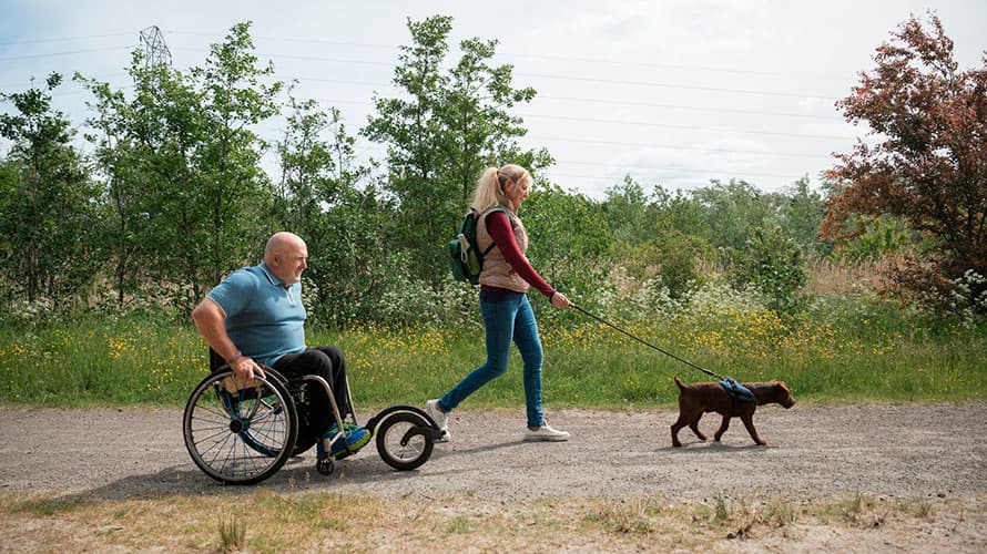 A wheelchair user enjoying a walk on an accessible trail with his partner and dog