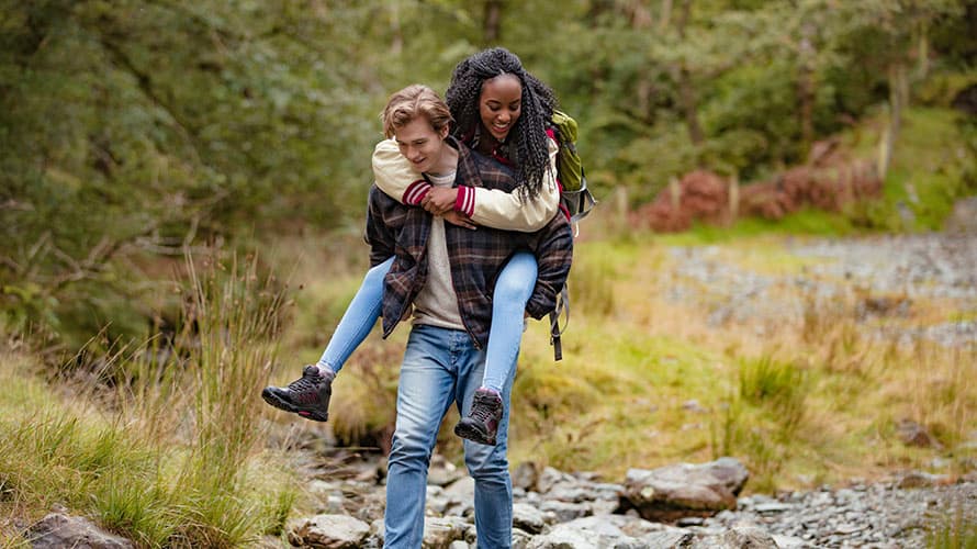 Couple piggybacking across a stream on a hike