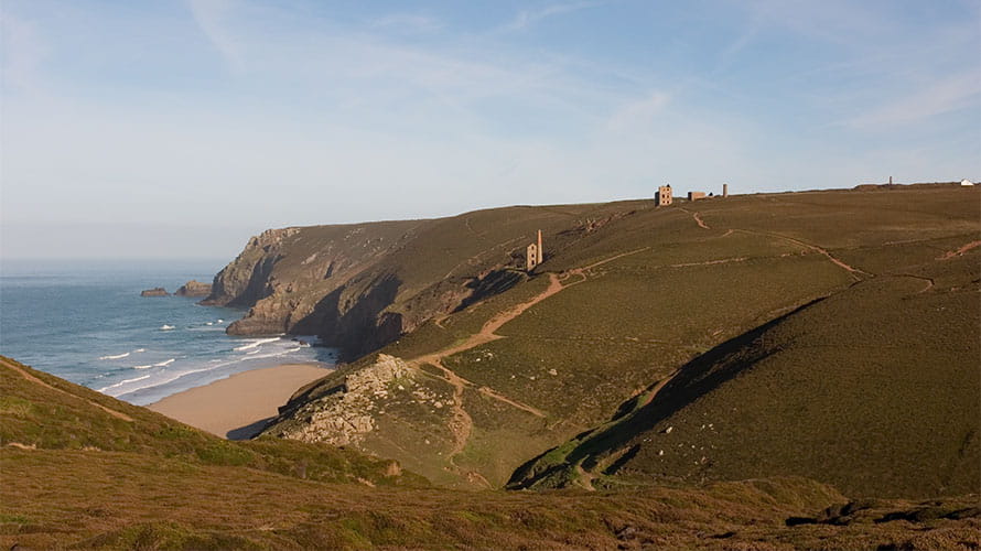 A view of the cliffs surrounding Chapel Porth Beach in Cornwall, with the ruins of tin mine chimneys visible