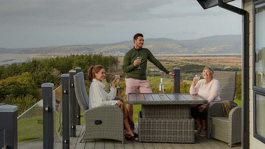 A family enjoying drinks on the veranda of their holiday lodge, overlooking the Welsh coast