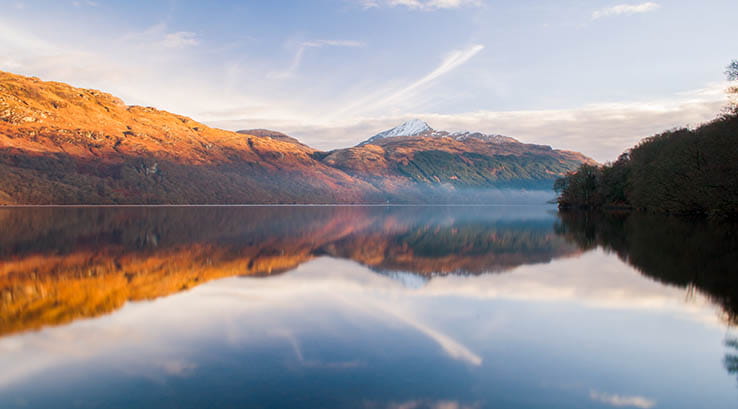 Glassy calm waters of Loch Lomond at sunrise