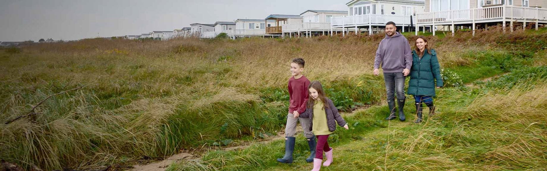 A family going for a walk through the grassy dunes from their caravan park
