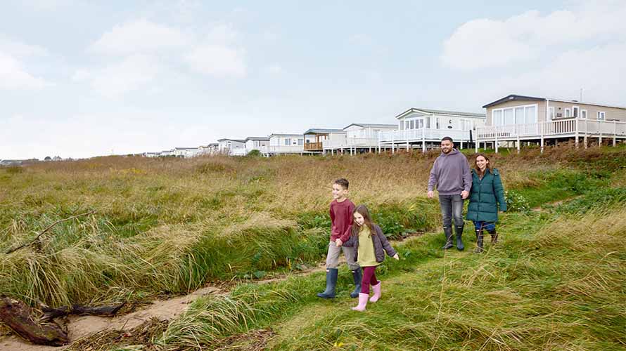 A family going for a walk through the grassy dunes from their caravan park
