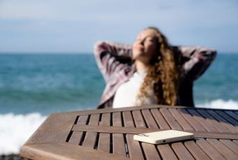 A woman relaxing by the beach with her phone face down on the table