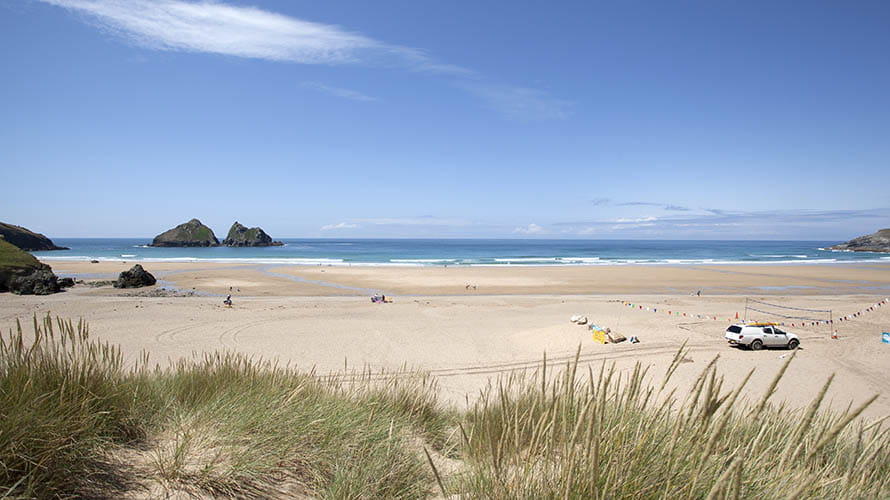 Lifeguards patrolling Holywell Bay Beach with distinctive Gull Rock visible on the horizon
