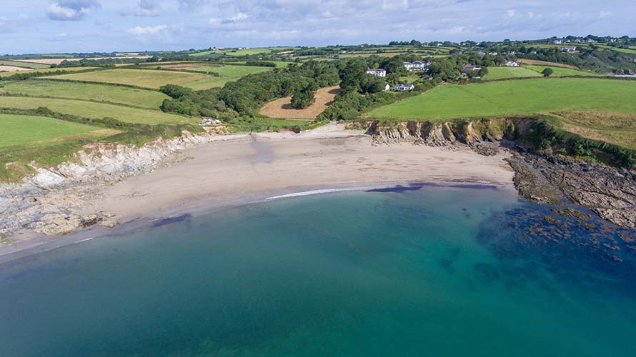 An aerial view of Porthcurnick Beach's crystal clear waters and white sands