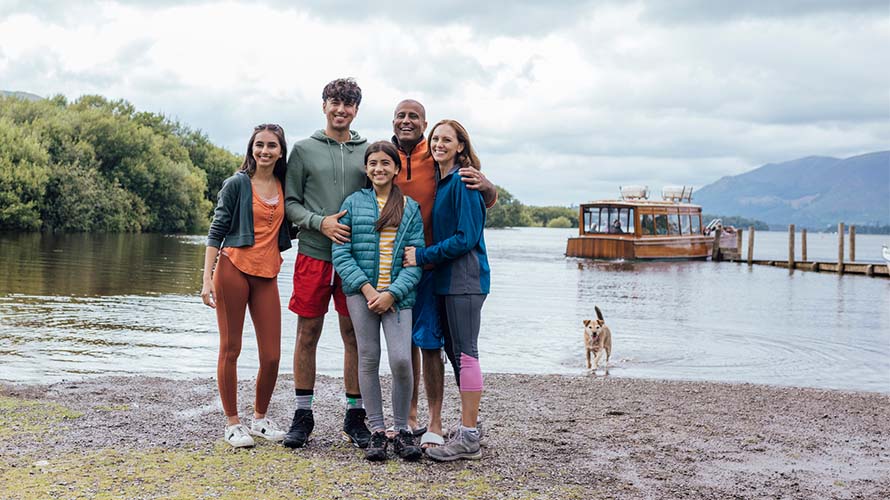 A family posing for a photo in front of the lake in Keswick, with their dog paddling in the water behind