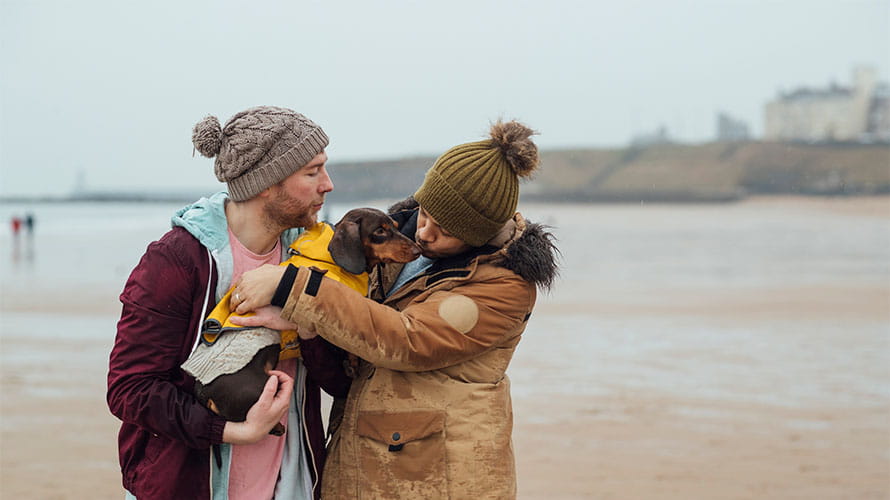 A couple cuddling their dog on a walk along the beach in Tynemouth