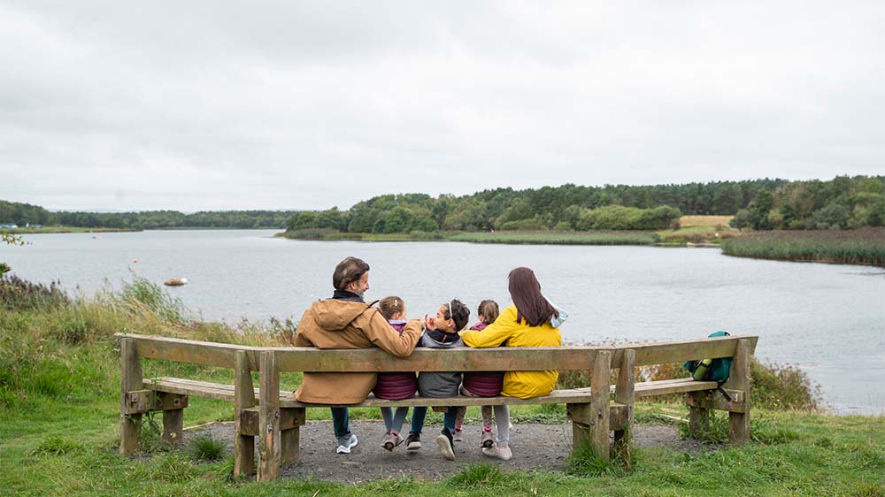 A family sitting on a bench overlooking a lake on a nature reserve